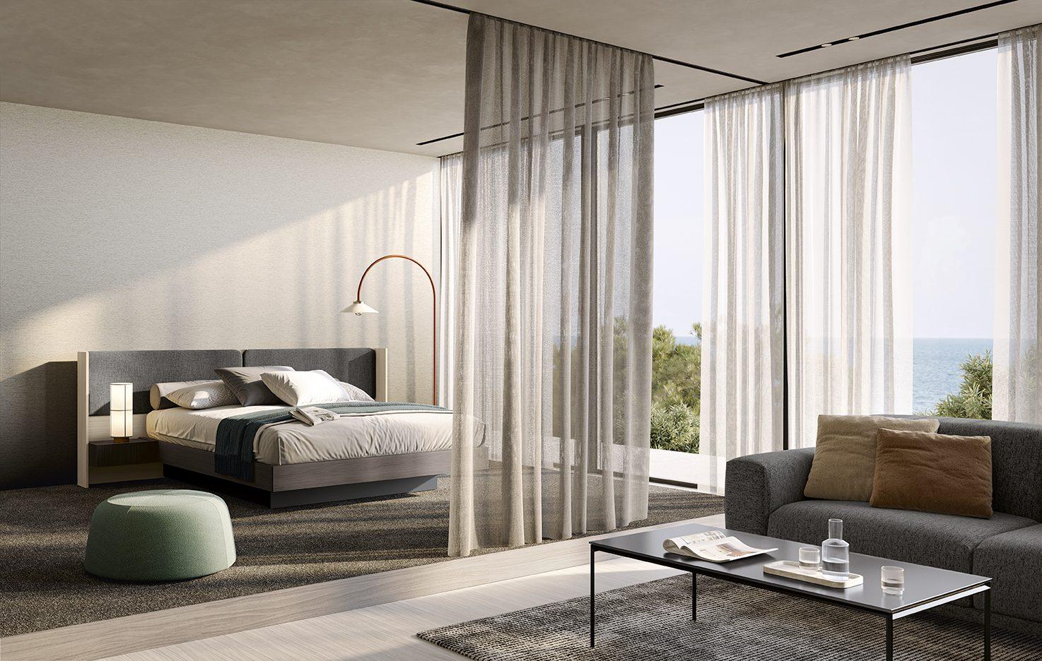 Suite hotel vista mare con letto imbottito grigio, testiera alta e zona living con divano e tavolino separati da tende leggere