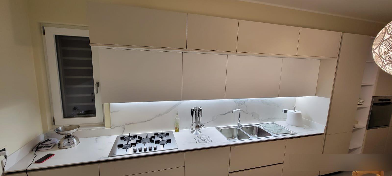 Cucina lineare beige con piano cottura, lavello e finestra
