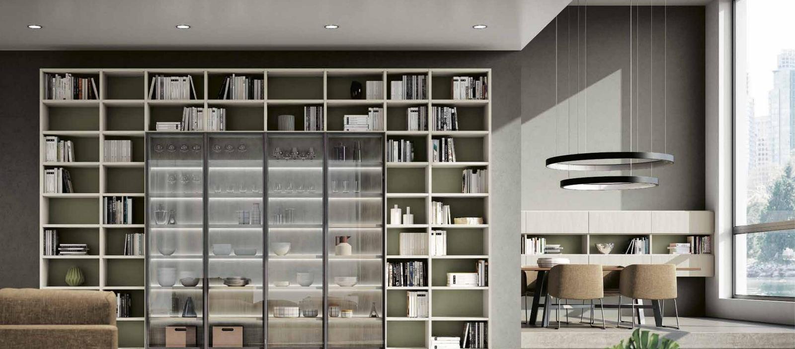 Libreria a giorno con vetrine a vista illuminate, ripiani in legno chiaro e fondali verde oliva